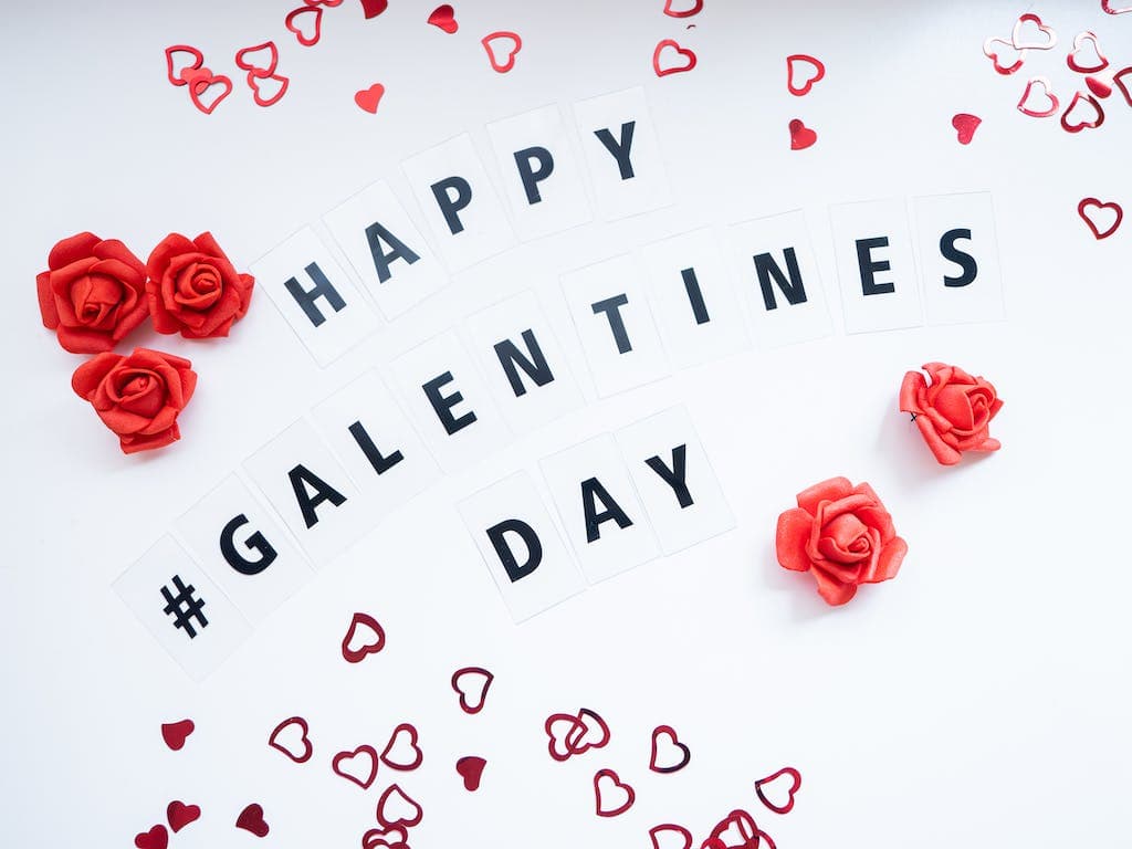 Message "Happy Galentine's Day" on a table with red roses and heart confetti